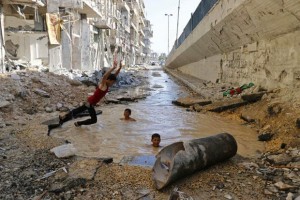 Crianças se banham na água aflorada em cratera de bomba, em Alepo, na Síria